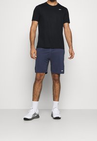 Camiseta negra de manga corta, pantalones cortos azul marino, zapatillas deportivas blancas y calcetines. Cuenta con un pequeño logo en la camiseta y costuras detalladas en los pantalones cortos.