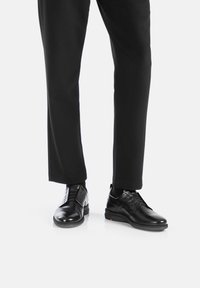 Scarpe eleganti in pelle nera con finitura liscia, design con lacci e suola in gomma. Abbinate a pantaloni neri per un aspetto formale.