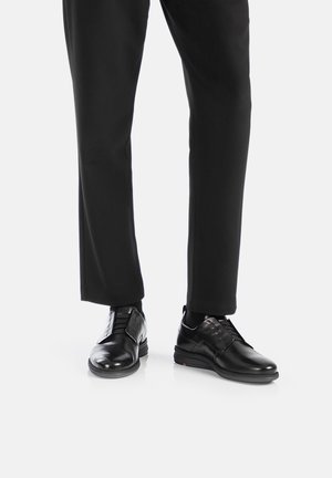 Black leather dress shoes with a smooth finish, lace-up design, and rubber sole. Paired with black trousers for a formal appearance.