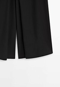 Pantalon noir à jambes larges avec un pli doux au bas de l'ourlet sur fond blanc.