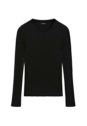 Donna che indossa una maglia nera a maniche lunghe, una lunga gonna nera, ballerine nere, occhiali da sole, porta una piccola borsa nera, in piedi su uno sfondo semplice.