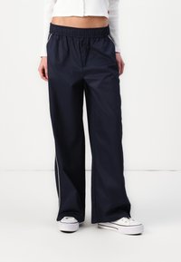 Marineblaue, weit geschnittene Hose aus leichtem Stoff, mit elastischem Bund und seitlichen Paspelierungen. Kombiniert mit weißen Sneakern.