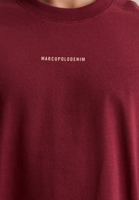 Burgunderfarbener Sweatshirt aus Baumwolle, mit einem gerippten Halsausschnitt und dem Text "MARCO POLO DENIM" in cremefarbe auf der Vorderseite.