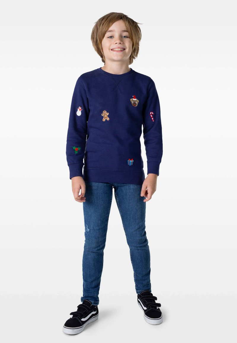 Marinblå sweatshirt med rund hals och broderade festliga motiv, inklusive en snögubbe och pepparkaksgubbe, kombinerad med blå jeans och svarta sneakers.