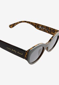 Okulary przeciwsłoneczne w panterkę z szarym przodem i czarnymi zausznikami. Posiadają zaokrąglone soczewki i złoty napis na jednym z zauszników.