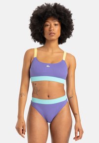 Lilla stripete bikini-sett med et crop-top med gule stropper og en aqua blå midjebånd på bunnene. Glatt tekstur, minimale design detaljer.