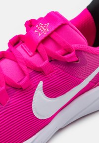 Baskets de sport roses vives en tissu texturé, avec un swoosh Nike blanc proéminent et une étiquette en forme d'étoile étiquetée "Star Runner". Présente un design en couches.