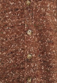 Texturerad brun cardigan med flerfärgade prickar, med fyra runda beige knappar och ett stickat mönster.