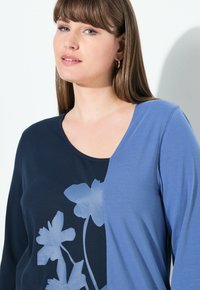 Blaue und marineblaue langärmlige Bluse mit floralem Muster, runder Ausschnitt, strukturierter Stoff auf einer Seite, glatter Stoff auf der anderen Seite und lässiger Schnitt.