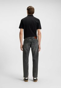 Polo nero con colletto abbinato a jeans in denim grigi. Caratteristiche notevoli includono una toppa in pelle con logo e sneakers nere con un accento bianco.