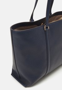 Sac en cuir bleu marine avec une finition texturée, offrant un intérieur spacieux, des doubles poignées et des accents en métal doré.