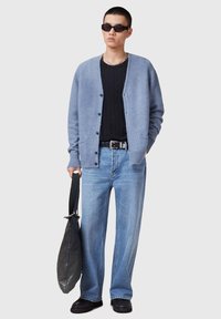 Cardigan di lana blu chiaro, camicia nera testurizzata, jeans blu chiaro larghi, borsa scura e scarpe nere. Outfit strutturato e casual con hardware minimale.