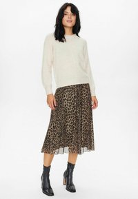 Krémový sveter s dlhými rukávmi, skombinovaný s voľnou midi sukňou s leopardím vzorom a čiernymi členkovými čižmami so zvýšeným podpätkom.