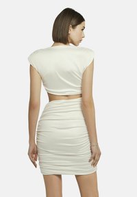 Witte, aansluitende jurk met een cropped top en gerimpelde textuur. Kenmerkt zich door korte mouwen en een uitsnijding op de rug. Gladde, lichte stof.