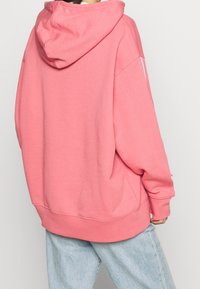 Růžová mikina s kapucí a volným střihem, vyrobená z měkké směsi bavlny. Obsahuje klokanku a pružné manžety.