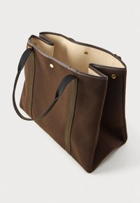 Καφέ υφασμάτινη τσάντα tote με αντίθετους μαύρους και ελαιόχρους ιμάντες, που διαθέτει χρυσές λεπτομέρειες και κρεμ εσωτερικό.