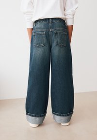 Modré džínsové nohavice širokých nohavíc s vysokým pásom, s dvoma zadnými vreckami a zahnutými manžetami, vyrobené z klasickej, textúrovanej látky.