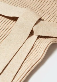 Tissu tricoté côtelé beige avec une large ceinture assortie nouée en un simple nœud sur une surface plane.
