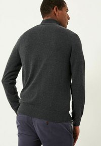 Dunkelgrauer Strickpullover mit hohem Kragen, gerippten Bündchen und Saum, der eine glatte Textur und eine schmale Passform aufweist. Kombiniert mit marineblauen Hosen.