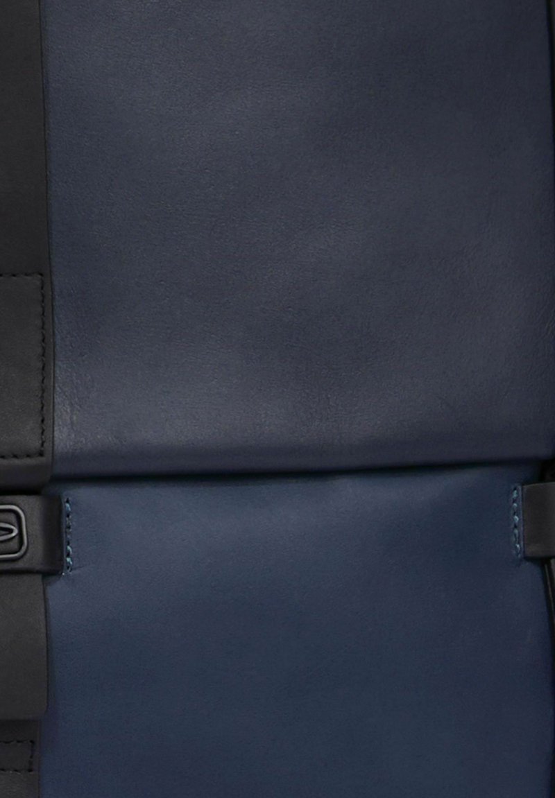 Borsa in pelle blu navy con texture liscia, dotata di una tracolla nera e accessori metallici; forma rettangolare, design minimalista.