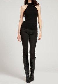 Haut à col halter noir à côtes associé à un pantalon ajusté en daim noir et des bottes noires imprimées crocodile montant jusqu'aux genoux. Texture lisse sur l'ensemble.