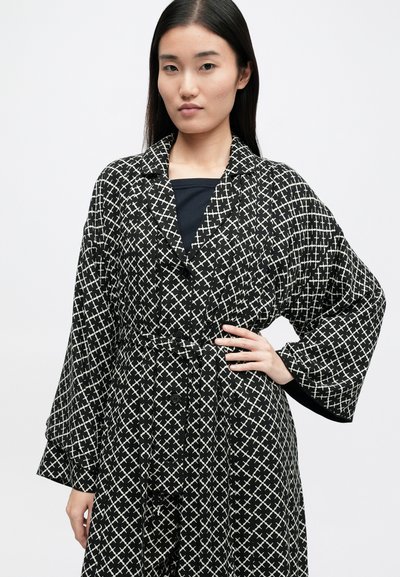 Μαύρη και λευκή ριγέ ρόμπα με σφιχτή μέση, μεγάλα μανίκια και κουμπιά μπροστά. Το ύφασμα έχει γεωμετρικό σχέδιο σταυροβελονιάς.