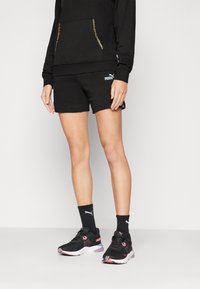 Sweatshirt atlético preto com detalhes em dourado, calções pretos, meias pretas com logo, e sapatilhas de corrida pretas com detalhes em rosa e branco.