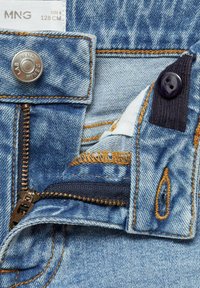 Denim kavbojke s svetlo modrim pranjem, ki imajo kovinsko gumbno zapiranje, mesingast zadrgo in kontrastno oranžno šivanje na robovih žepov.