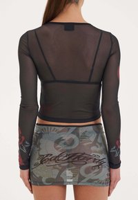 Schwarzes, langärmliges Oberteil aus Mesh mit einer taillierten Silhouette; die Ärmel sind mit floralem Print versehen. Der Rock hat ein buntes, gemustertes Design mit Textdetails.