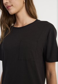 Czarny bawełniany T-shirt z okrągłym dekoltem, krótkimi rękawami i kieszonką na lewej piersi z wytłaczanym logo, gładka faktura.