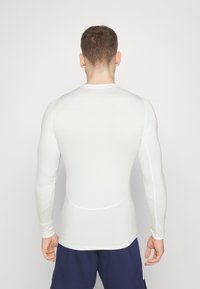 Langarmige witte sportshirt met een gladde textuur, een strakke pasvorm en platte naden. De achterkant toont een eenvoudige, naadloze look.
