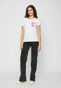 White cotton t-shirt with short sleeves, featuring "WAITING FOR FRIDAY" in pink text on the front. Paired with dark jeans and sneakers.