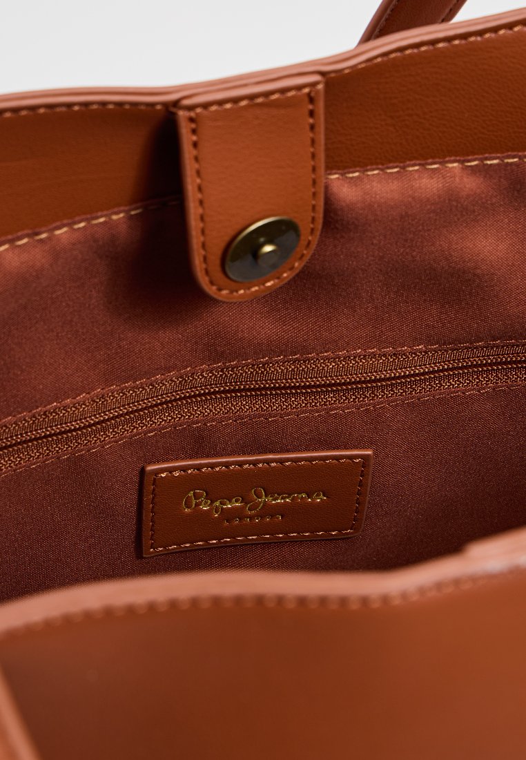 Interior de un bolso de mano de cuero marrón con un forro suave y satinado, un bolsillo con cremallera y una etiqueta de marca con letras doradas.