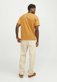 Kratkoroč T-shirt v senfu barvi iz bombaža, v kombinaciji z svetlobezhnimi širokimi hlačami in rjavimi semiš čevlji. Preprost dizajn, brez vidnih vzorcev.