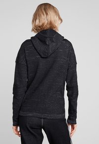 Czarna bluza z kapturem o teksturowanej tkaninie, luźnym kroju i długich rękawach. Zawiera subtelny wzór oraz sznurek do ściągania kaptura.