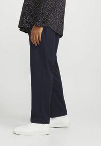 Pantalons à rayures marines en tissu texturé, associés à des baskets blanches. La chemise présente un petit motif floral.