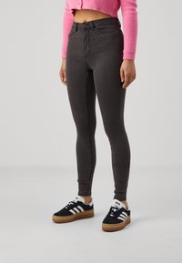Person som bär högmidjade mörkgrå slim-fit jeans, svarta och vita Adidas-sneakers, samt en kort ljusrosa fluffig tröja.