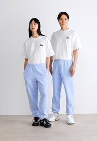 Camisetas de algodón blancas con un pequeño logo verde, combinadas con pantalones de chándal azul claro de corte relajado. Incluyen bolsillos laterales y cinturillas elásticas.