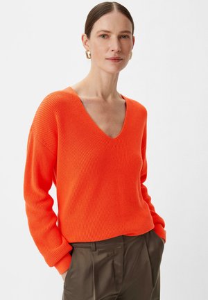 Sweter w serek, oversize, o intensywnym pomarańczowym kolorze, z prążkowaną strukturą i długimi rękawami, w połączeniu z spodniami o wysokim stanie w ciemnym kolorze.