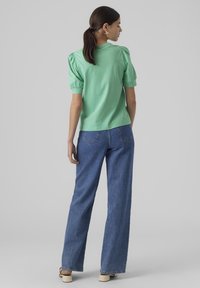Mintgrön kortärmad topp med puffärmar, kombinerad med raka blå denimjeans. Slät tyg med avslappnad passform.