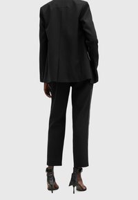 Black tailored blazer with a single vent, paired with black trousers featuring a side stripe, and black high-heeled ankle boots.