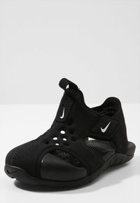 Svart atletisk sandal i flexibelt material, med stängd tå, utskurna sidor och en texturerad fotbädd. Nike-logotypen är synlig.
