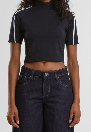 Zwarte cropped t-shirt met hoge kraag, korte mouwen en witte strepen op de schouders, gecombineerd met donkerdenim jeans met lichte stitching.