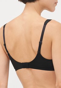 Soutien-gorge sans fil noir avec bretelles ajustables, fermeture à crochets et œillets, et tissu lisse. Présente un design simple sans embellissements.