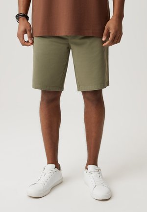 Oliwkowe szorty o prostym kroju, wykonane z bawełny, z pętelkami na pasek i bocznymi kieszeniami. W połączeniu z białymi trampkami.