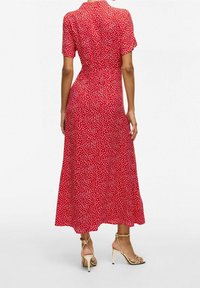 Robe rouge mi-longue à manches courtes, ornée d'un motif à pois blancs, avec une taille cintrée. Portée avec des talons dorés à brides.