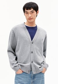 Cardigan gris avec un col en V, boutonnage à l'avant et poignets côtelés, associé à un t-shirt bleu à col rond en dessous. Texture lisse, coupe décontractée.
