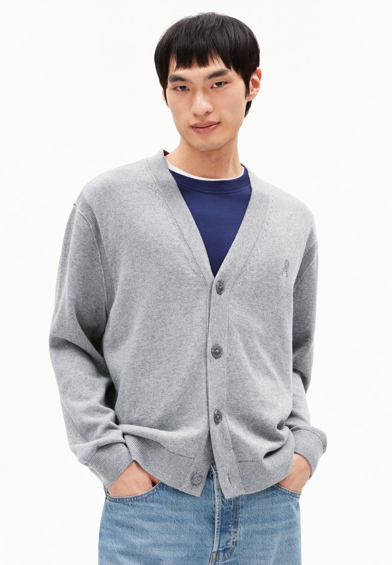 Cardigan gris avec un col en V, boutonnage à l'avant et poignets côtelés, associé à un t-shirt bleu à col rond en dessous. Texture lisse, coupe décontractée.