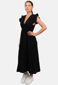 Zwarte maxi-jurk met een V-hals, korte gerimpelde mouwen en een gestructureerde stof. Gekocht met witte sneakers, met een uitlopende snit.