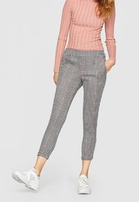 Pantalons à carreaux effilés en tissu noir et blanc avec une taille élastique. Portés avec un haut rose à côtes et des baskets blanches.